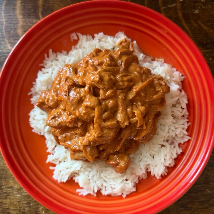 Butter chicken on basmati rice, on a red plate.