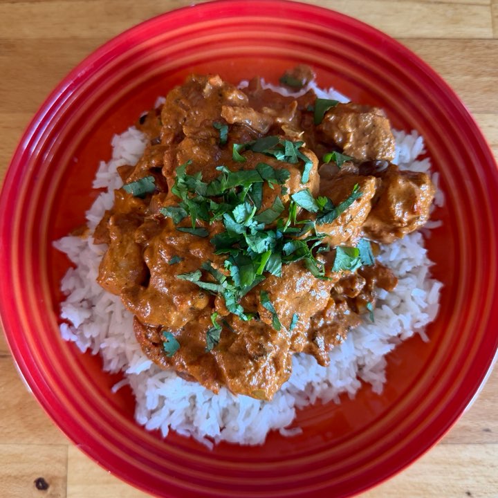 Chicken tikka masala on rice with coriander, on a red plate.