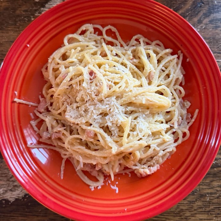 Spaghetti carbonara with grated cheese, on a red plate.